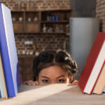 student hiding behind bookshelf