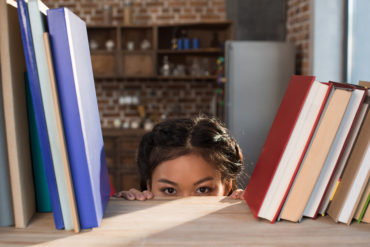 student hiding behind bookshelf